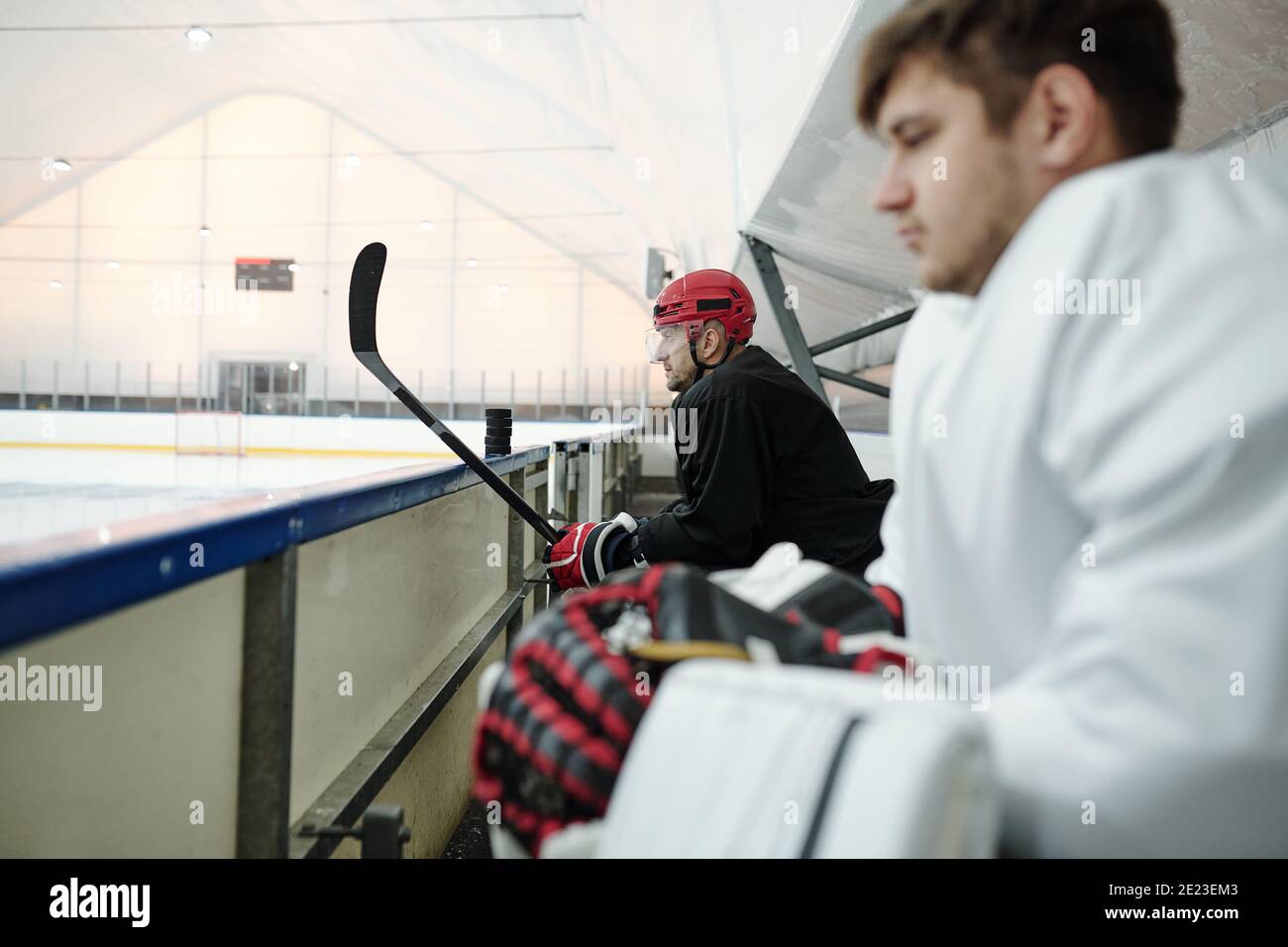 Vue latérale de deux joueurs de hockey assis sur un uniforme de sport dans la première rangée de la tribune devant large stade moderne tout en faisant une pause Banque D'Images