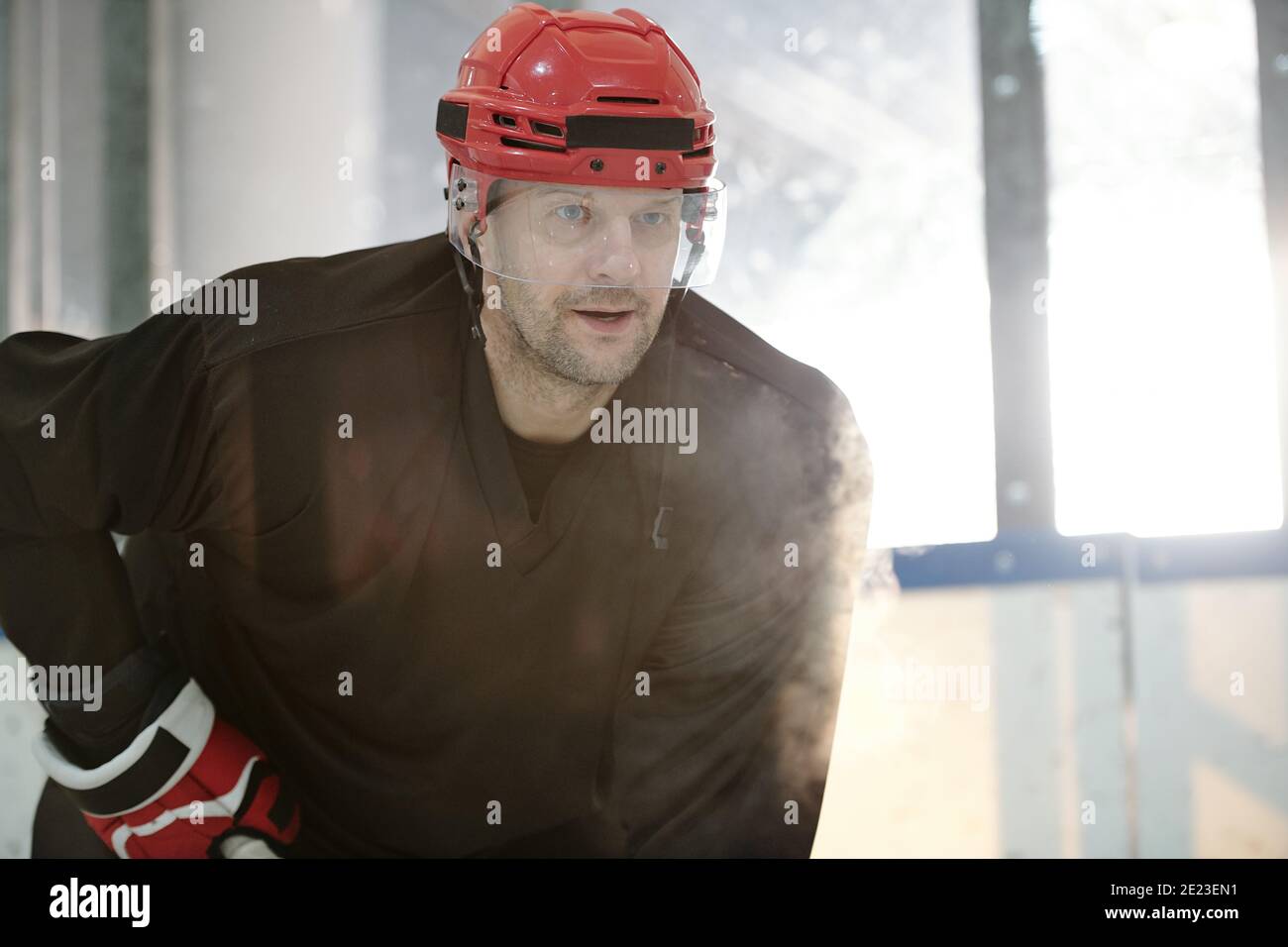 Joueur de hockey mature en uniforme sportif, casque de protection et gants debout sur la patinoire du stade en attendant le palet de rival Banque D'Images