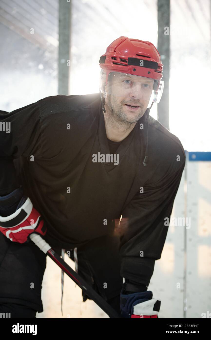 Joueur de hockey mature en uniforme sportif, casque de protection et gants tenant le bâton en se tenant debout sur la patinoire et en attendant le palet Banque D'Images