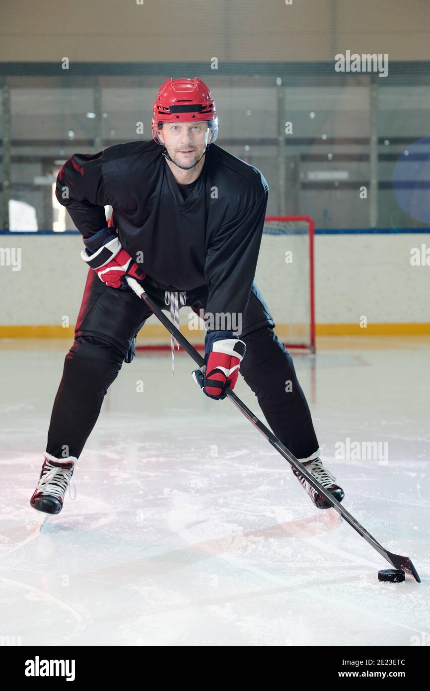 Joueur de hockey mûr avec casque et gants de protection descendant faites une patinoire devant l'appareil photo et regardez-vous pendant que vous êtes en train de le regarder va tirer sur le disque Banque D'Images