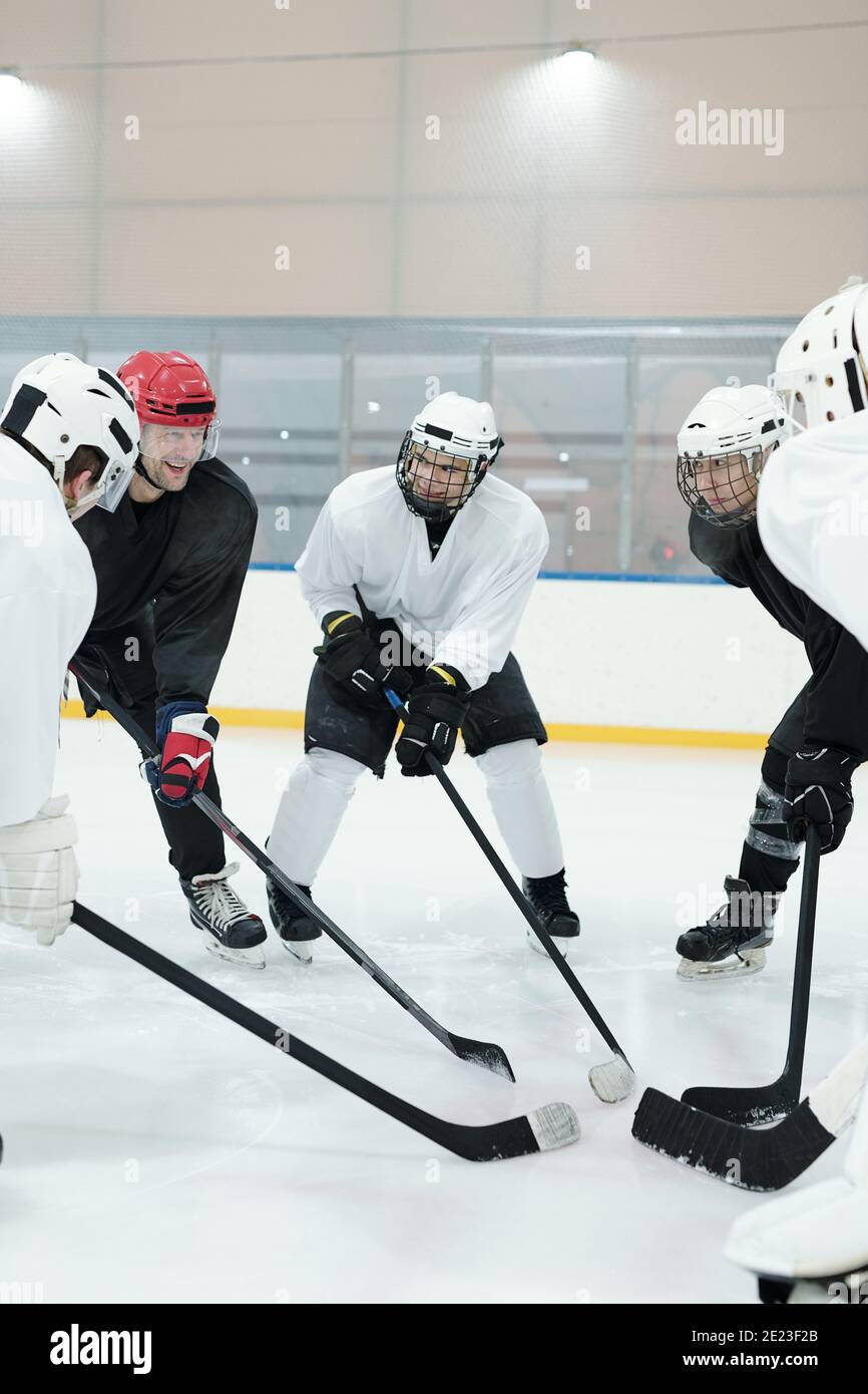 Groupe de joueurs de hockey professionnels en uniforme de sport, casques de protection, gants et patins debout en cercle sur la patinoire pendant l'entraînement avant pl Banque D'Images