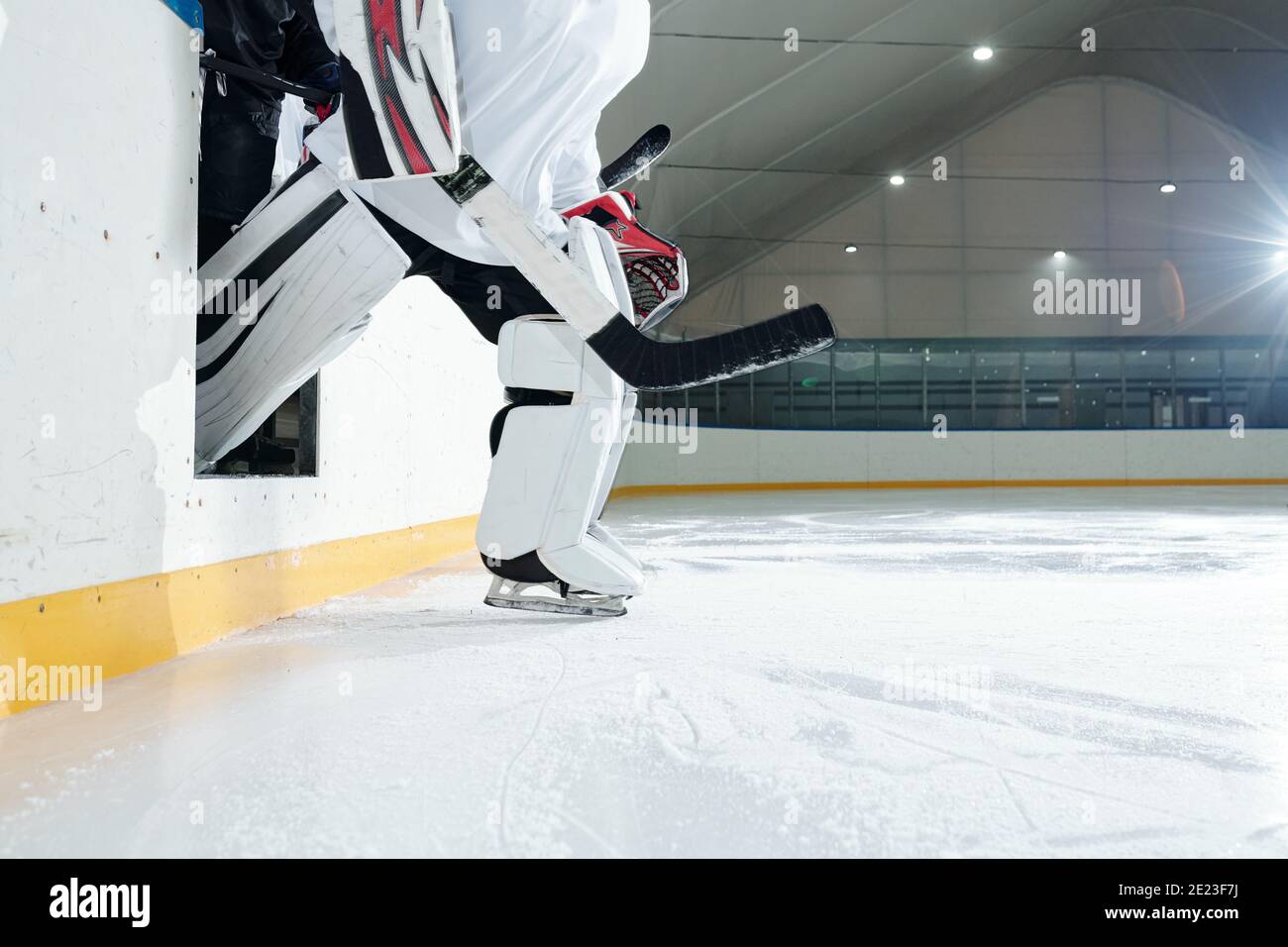 Joueur de hockey professionnel en uniforme, casque de protection, gants et patins sortant de la tribune à la patinoire pour jouer dans le stade tout en tenant le bâton Banque D'Images