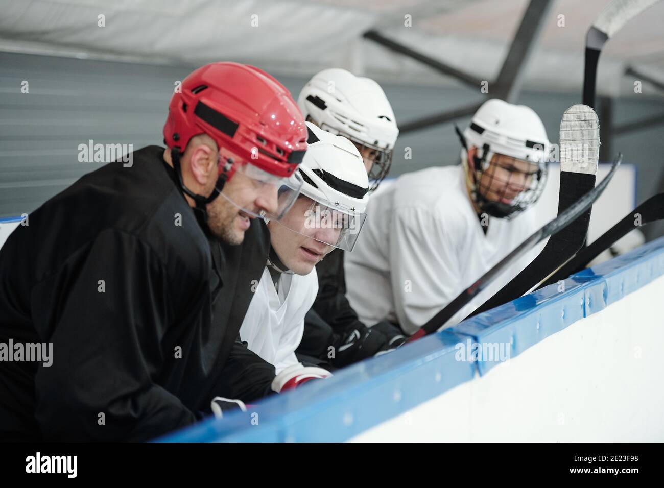 Groupe de jeunes joueurs de hockey en uniforme sportif tribune sur le stade et à l'écoute de leur entraîneur expérimenté pendant préparation pour la lecture Banque D'Images