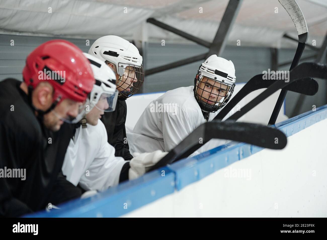 Groupe de jeunes joueurs de hockey en uniforme sportif et en casques assis sur la première rangée de tribune sur le stade pendant préparation pour la lecture Banque D'Images