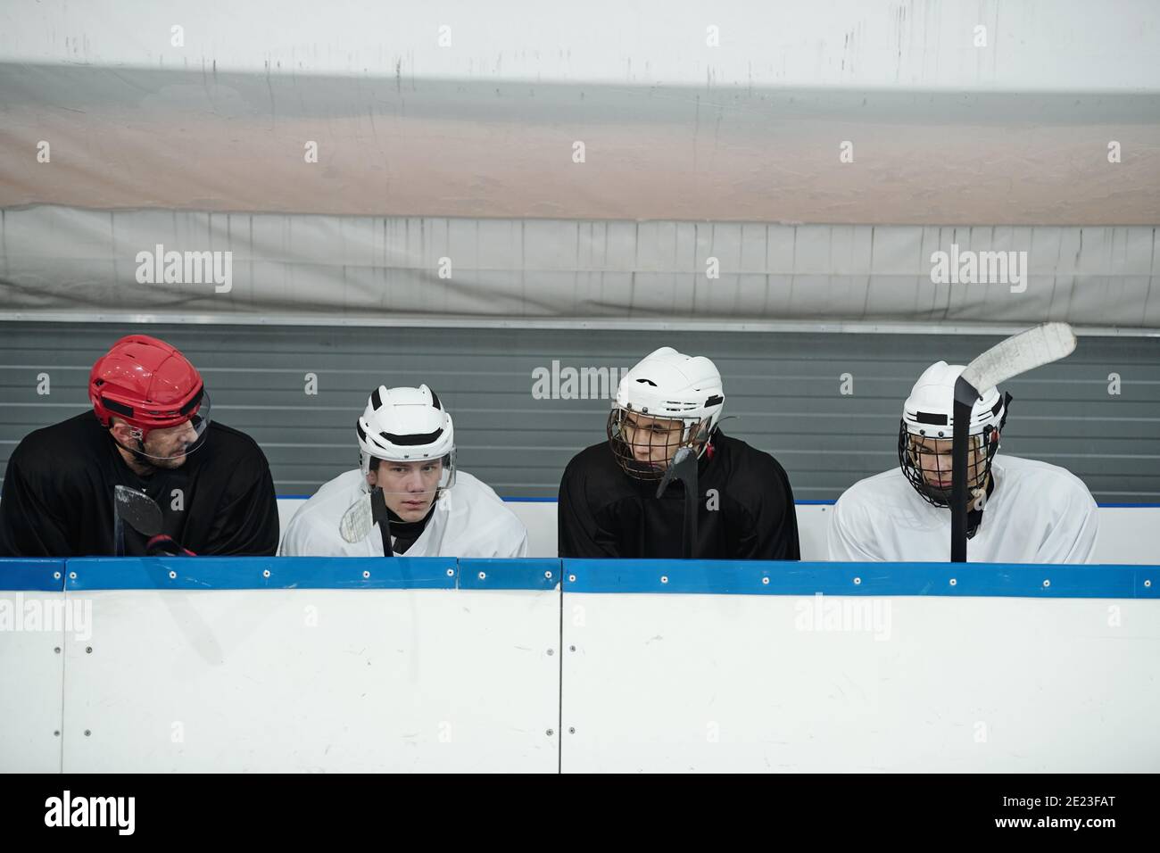 Groupe de jeunes joueurs de hockey et leur entraîneur dans le sport uniforme assis dans une tribune sur le stade pendant une pause ou préparation pour la lecture Banque D'Images