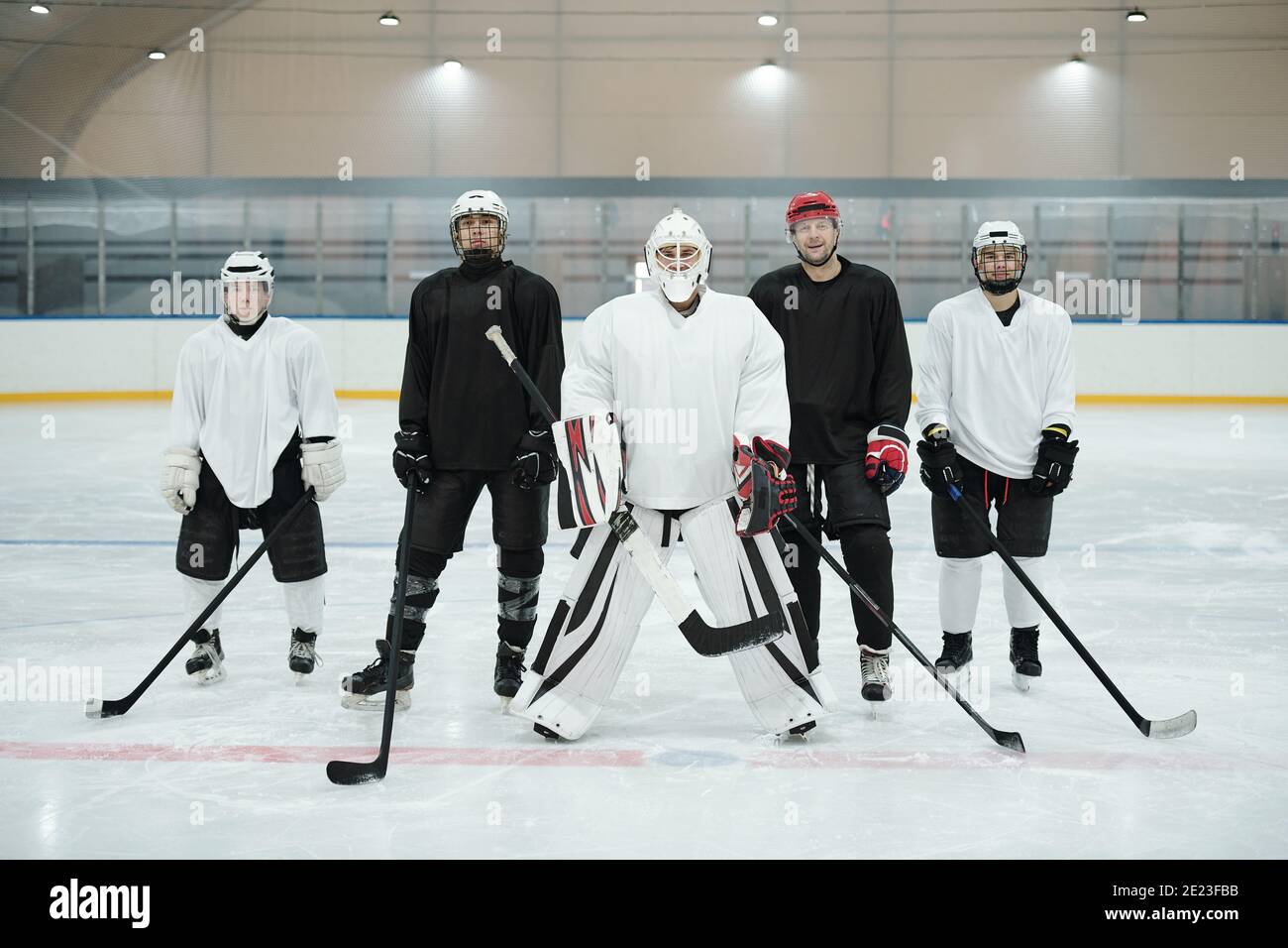 Joueurs de hockey professionnels et leur entraîneur en uniforme de sport, gants, patins et casques de protection debout sur la patinoire en attendant le jeu Banque D'Images