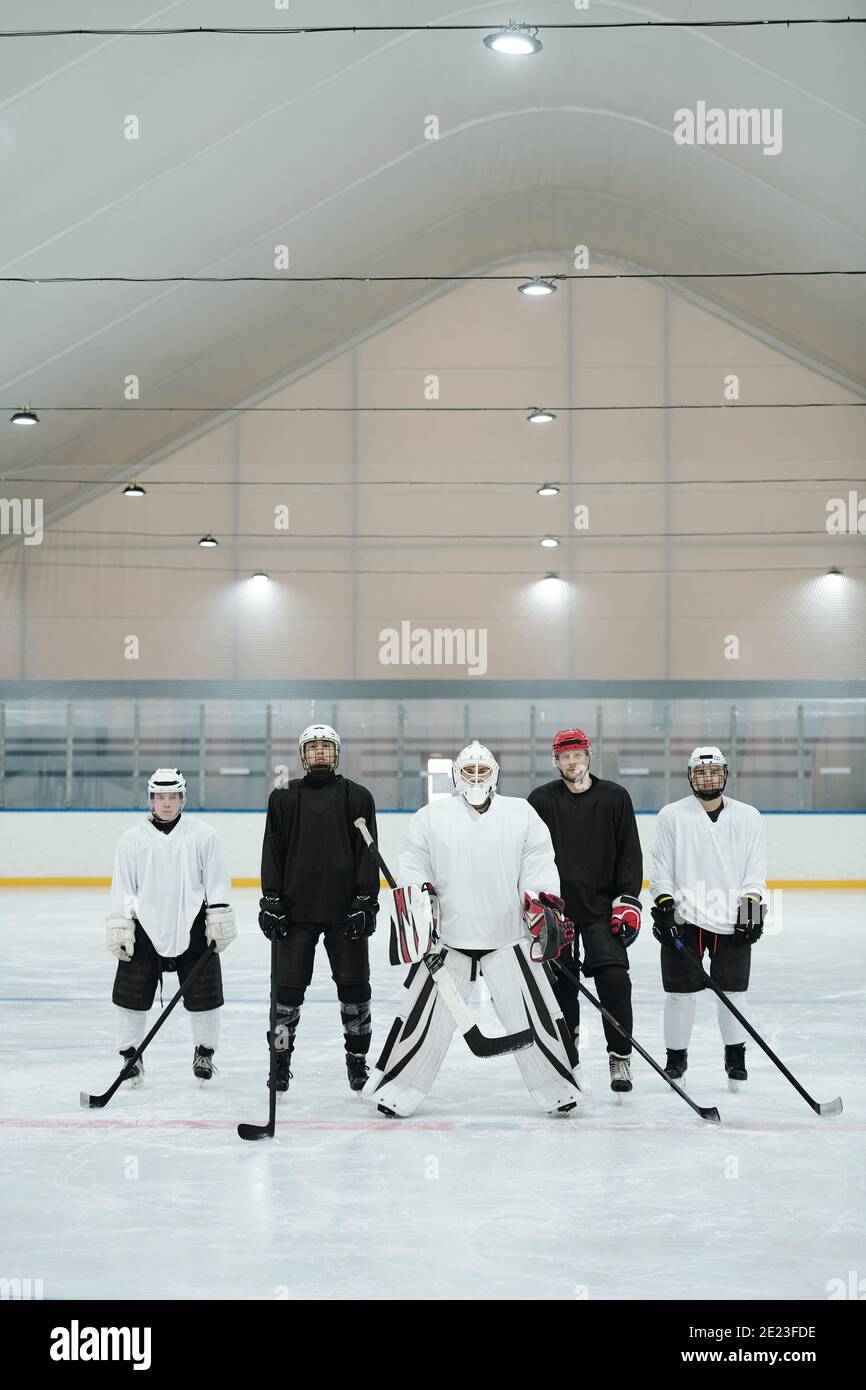Groupe de joueurs de hockey et leur entraîneur en uniforme sportif, gants, patins et casques de protection debout sur la patinoire en attendant le jeu Banque D'Images