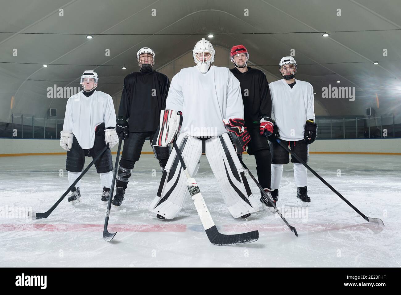 Joueurs de hockey professionnels et leur entraîneur en uniforme sportif, gants, patins et casques debout sur la patinoire et attendant le début du jeu Banque D'Images