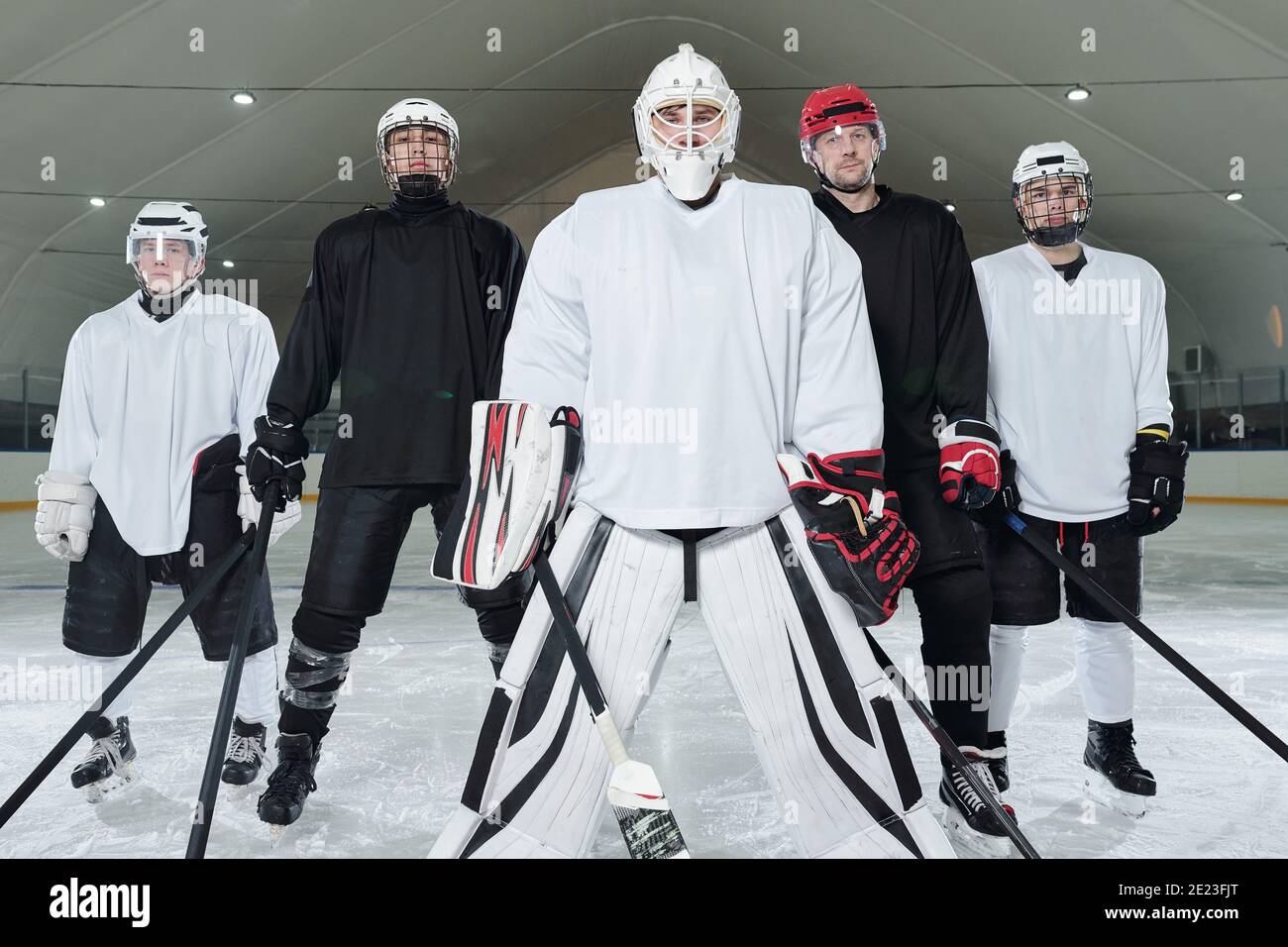 Joueurs de hockey professionnels et leur entraîneur en uniforme, gants, patins et casques debout sur la patinoire du stade et attendant le début du match Banque D'Images