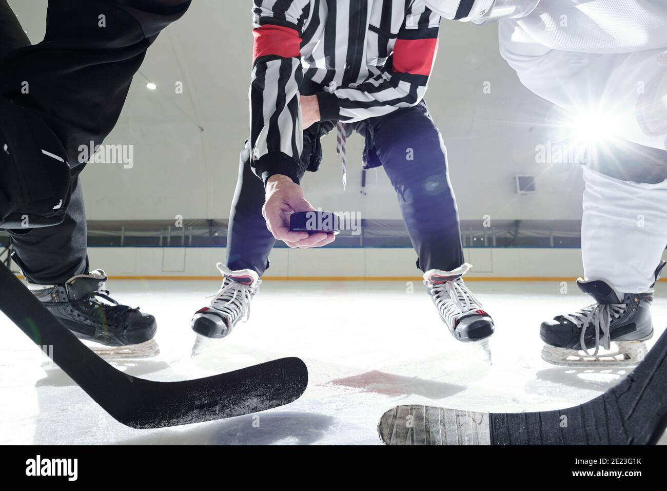 Arbitre de hockey avec rondelle debout sur la patinoire entre deux les joueurs avec des bâtons attendent le moment pour être le premier pour le tirer pendant l'entraînement Banque D'Images