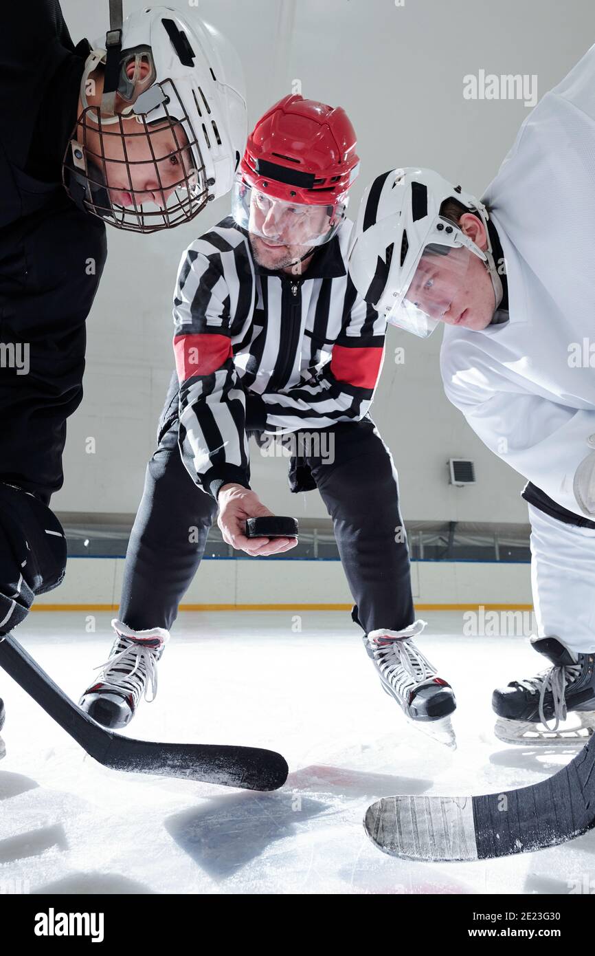 Arbitre de hockey tenant le palet sur la patinoire pendant que deux rivaux avec des bâtons regardant tout en se préparant à la tirer pendant la formation Banque D'Images