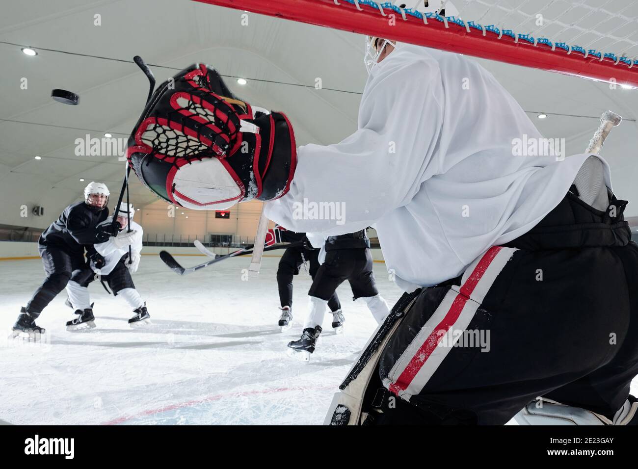 Vue arrière du joueur de hockey en uniforme de sport et gants se tenant dans le filet devant le groupe de rivaux et se préparer à attraper le galet Banque D'Images