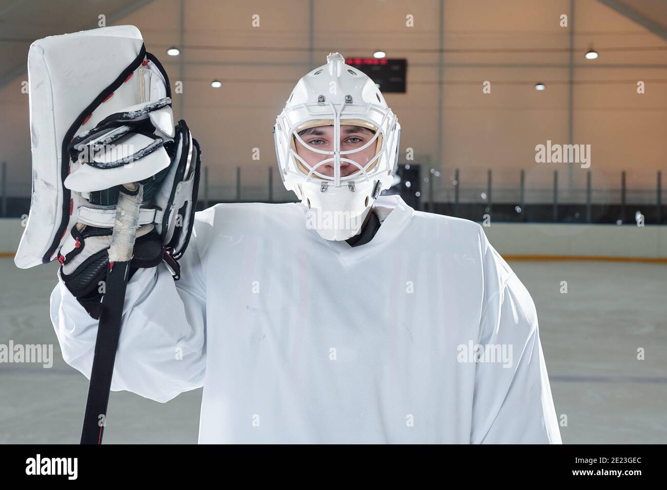 Jeune joueur de hockey en uniforme de sport, gants et casque de protection bâton de maintien et en se tenant sur la patinoire devant la caméra après le jeu Banque D'Images