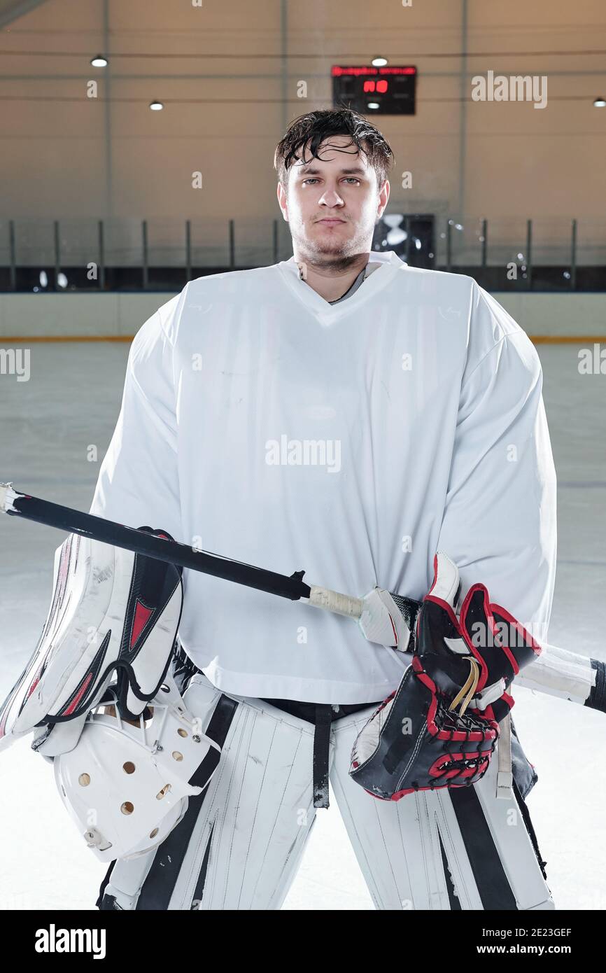 Jeune joueur de hockey sérieux en uniforme de sport et tenue de gants collez et portez un casque de protection en vous tenant sur la patinoire jouer ou s'entraîner Banque D'Images