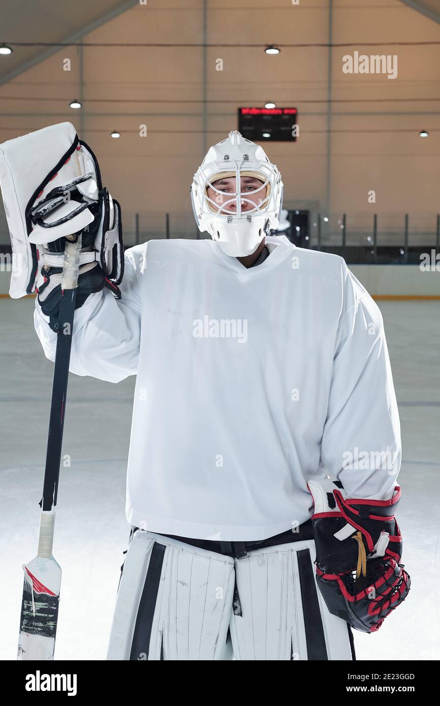 Jeune joueur de hockey professionnel en uniforme de sport, gants et bâton de maintien de casque de protection tout en se tenant sur la patinoire devant la caméra après pla Banque D'Images