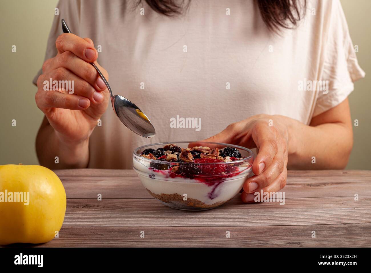 Une femme caucasienne mange un bol en verre frais fait maison de yaourt crémeux parfait avec des baies, muesli et des graines dans elle sur table en bois gros plan Banque D'Images