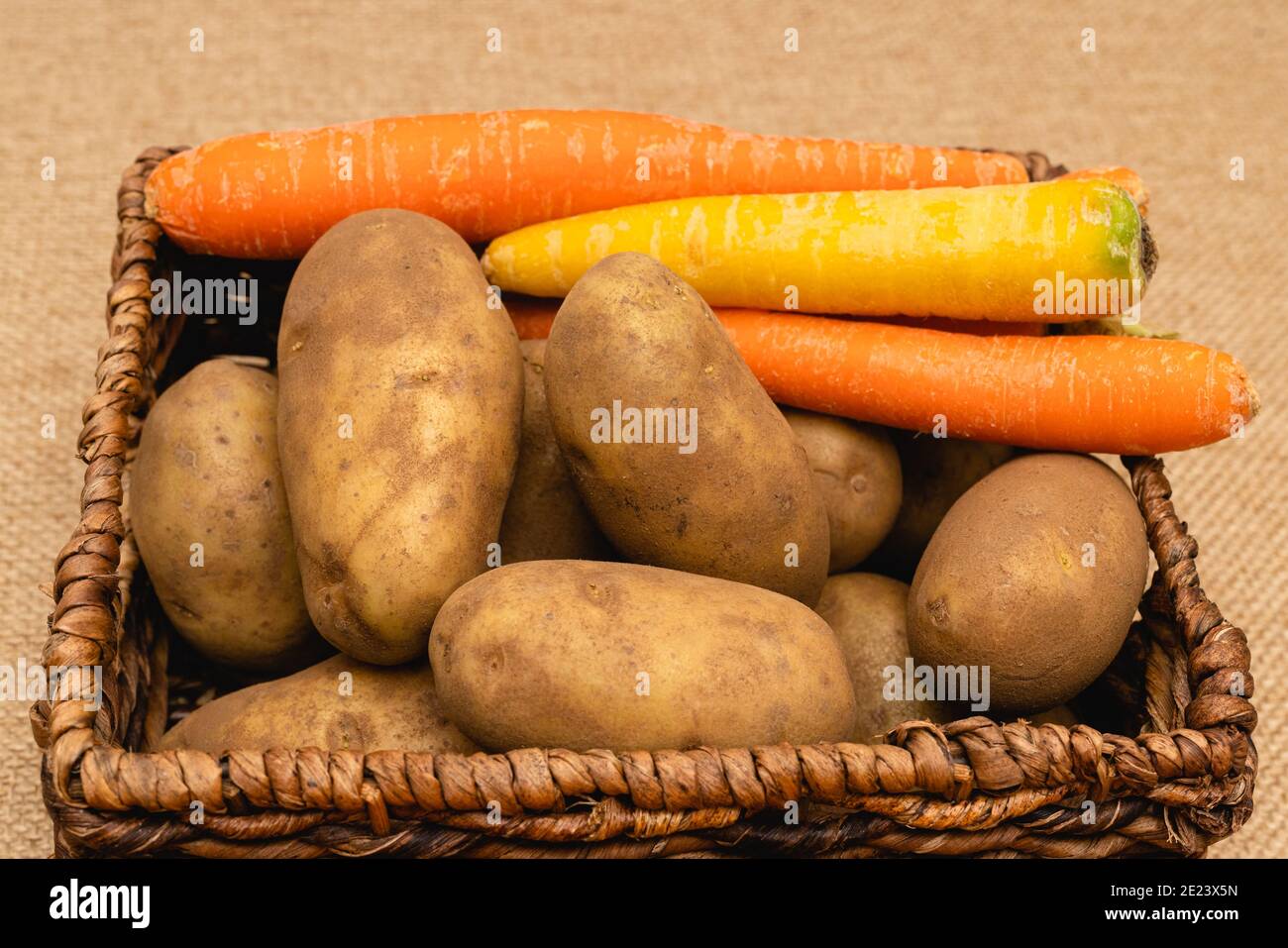 Les pommes de terre et les carottes biologiques sont rapprochées dans un panier arrière-plan rustique Banque D'Images