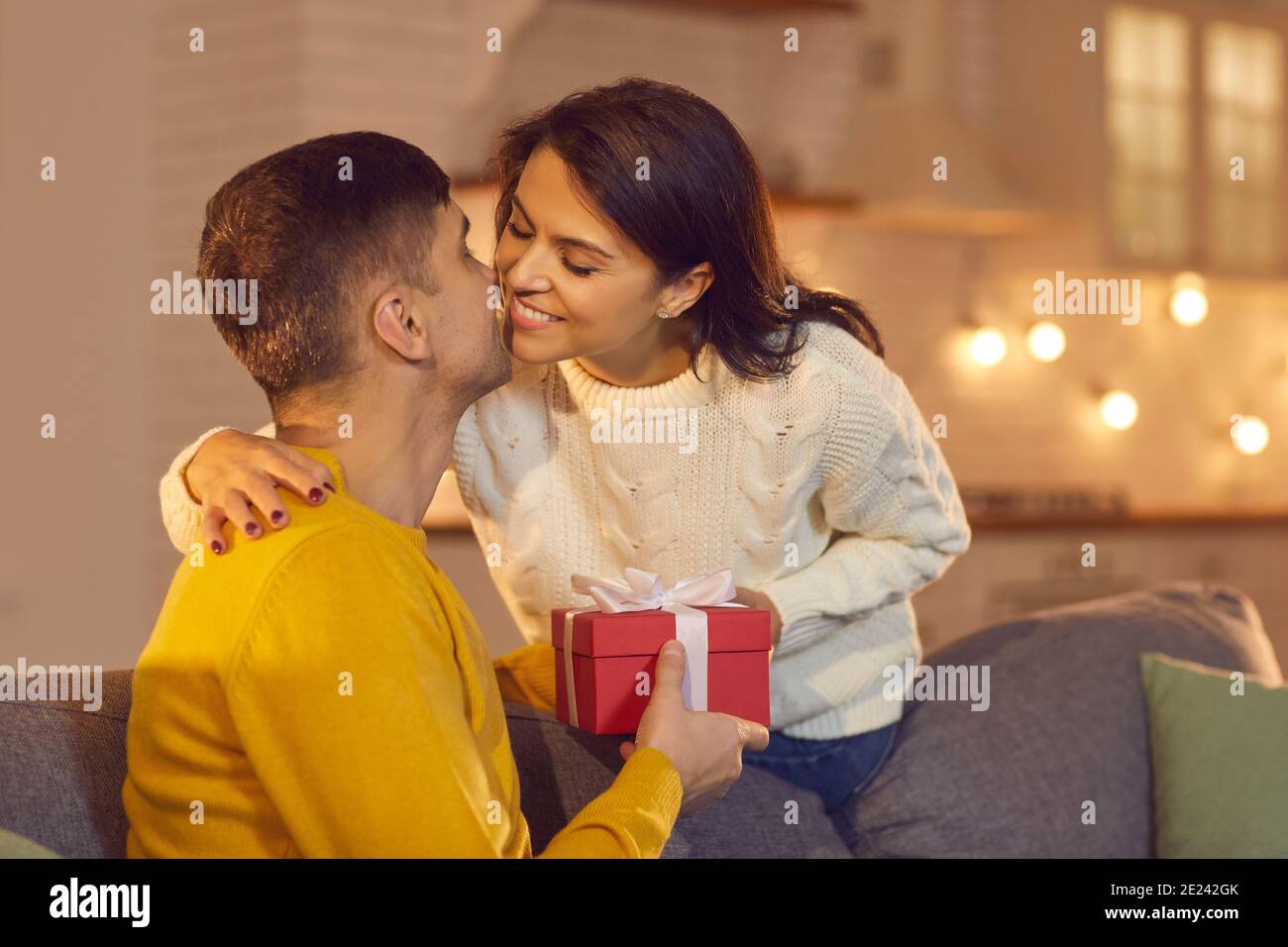 Couple souriant donnant des cadeaux et embrassant à la maison pendant la Saint-Valentin fête Banque D'Images