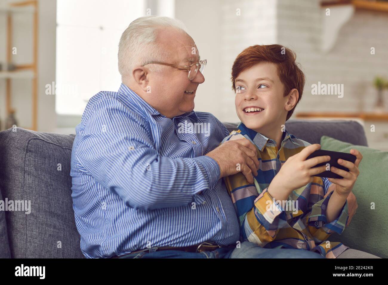 Petit-fils et grand-père heureux assis sur un canapé et jouant à des jeux sur un nouveau téléphone mobile Banque D'Images