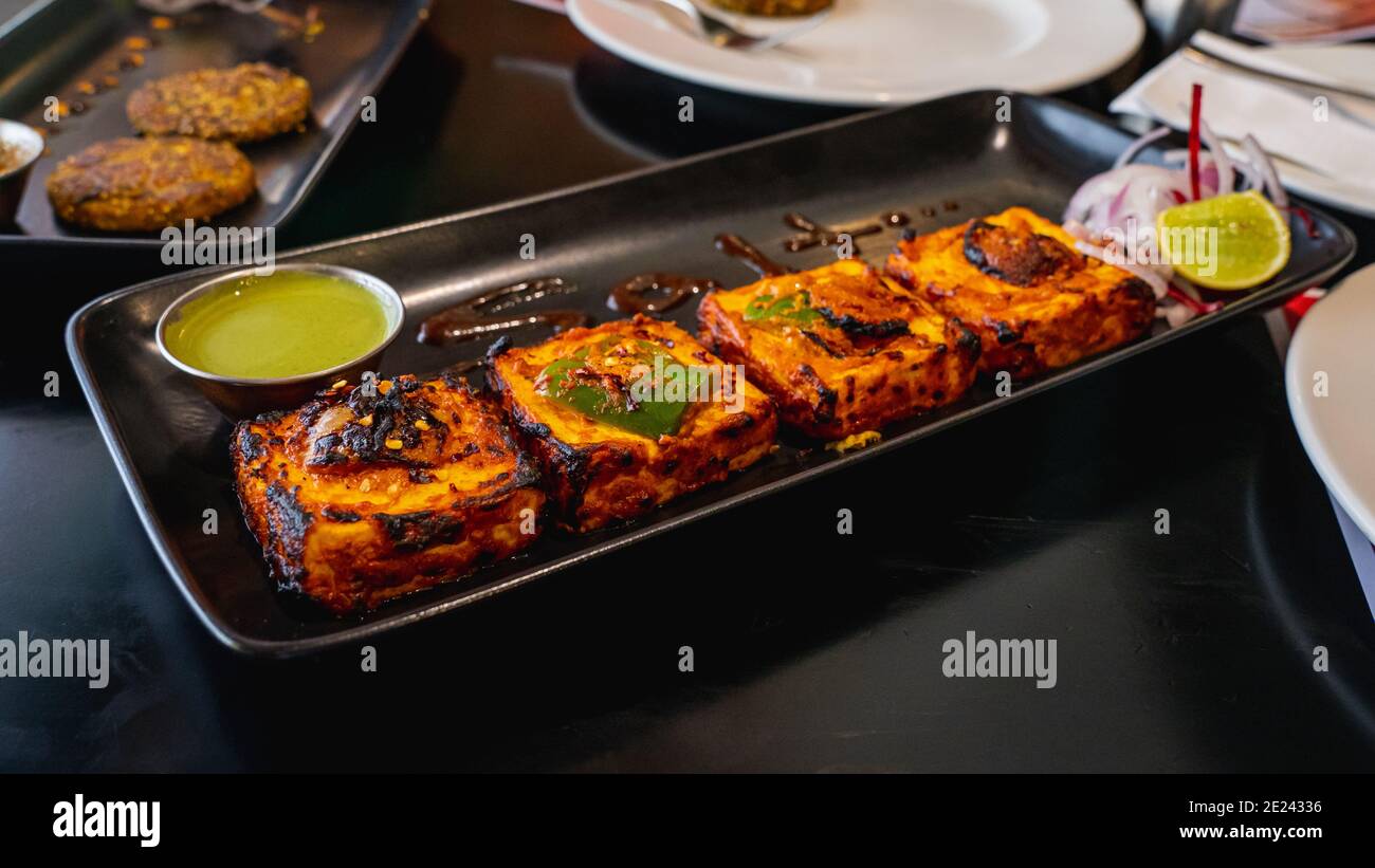Foyer sélectif de Paneer Tikka Kebab servi avec du chutney vert sur un plateau de service noir Banque D'Images Foyer sélectif de Paneer Tikka Kebab servi avec du chutney vert sur un plateau de service noir Banque D'Images