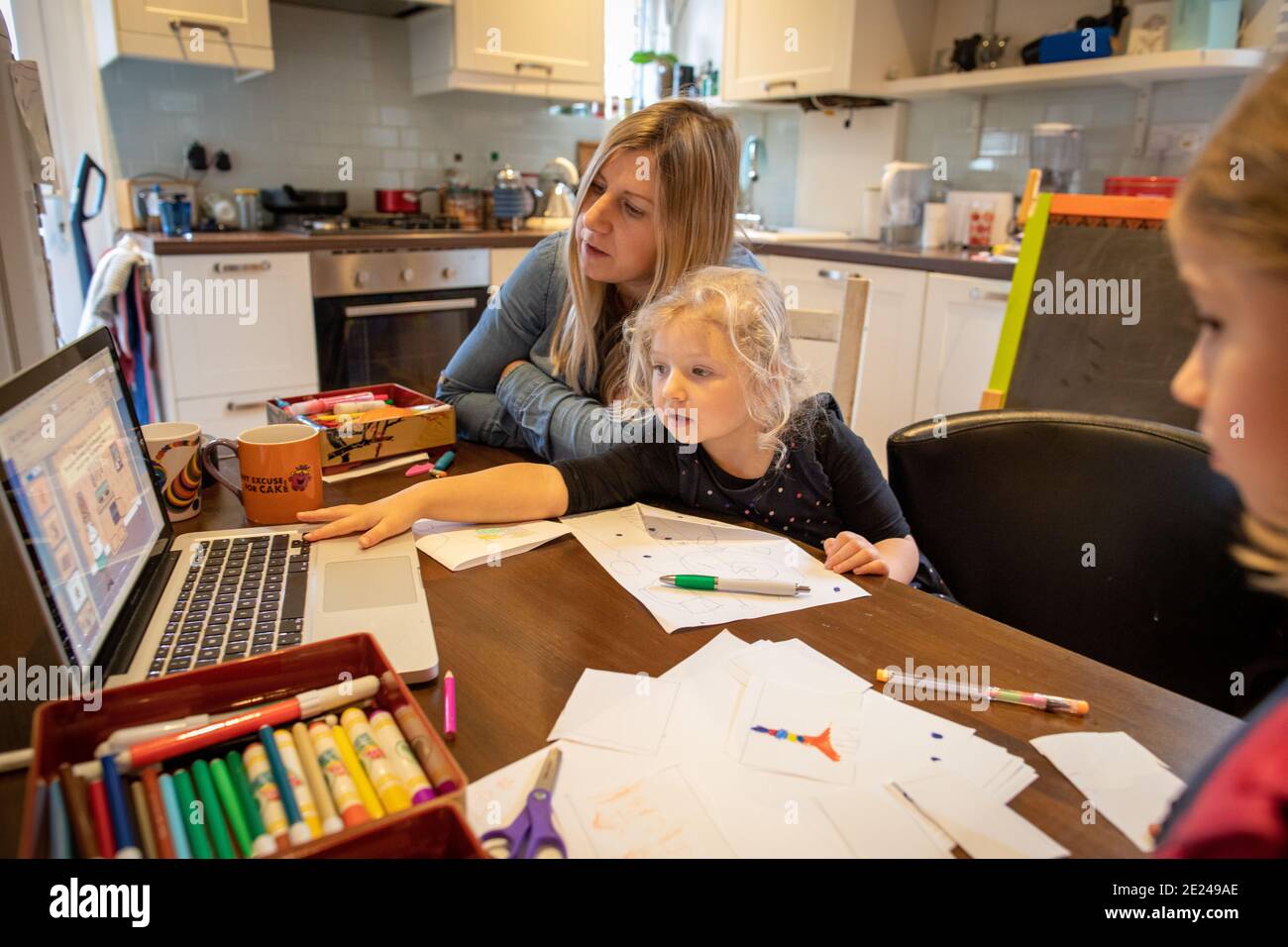 Une fille de trois ans qui apprend à la maison avec sa mère en utilisant un ordinateur portable sur la table de cuisine. Banque D'Images
