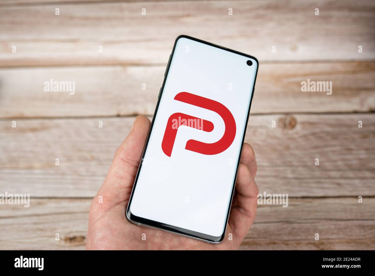 Homme tenant un smartphone avec le logo Parler, une application de réseau social à discours libre. Logo rouge sur fond blanc Banque D'Images