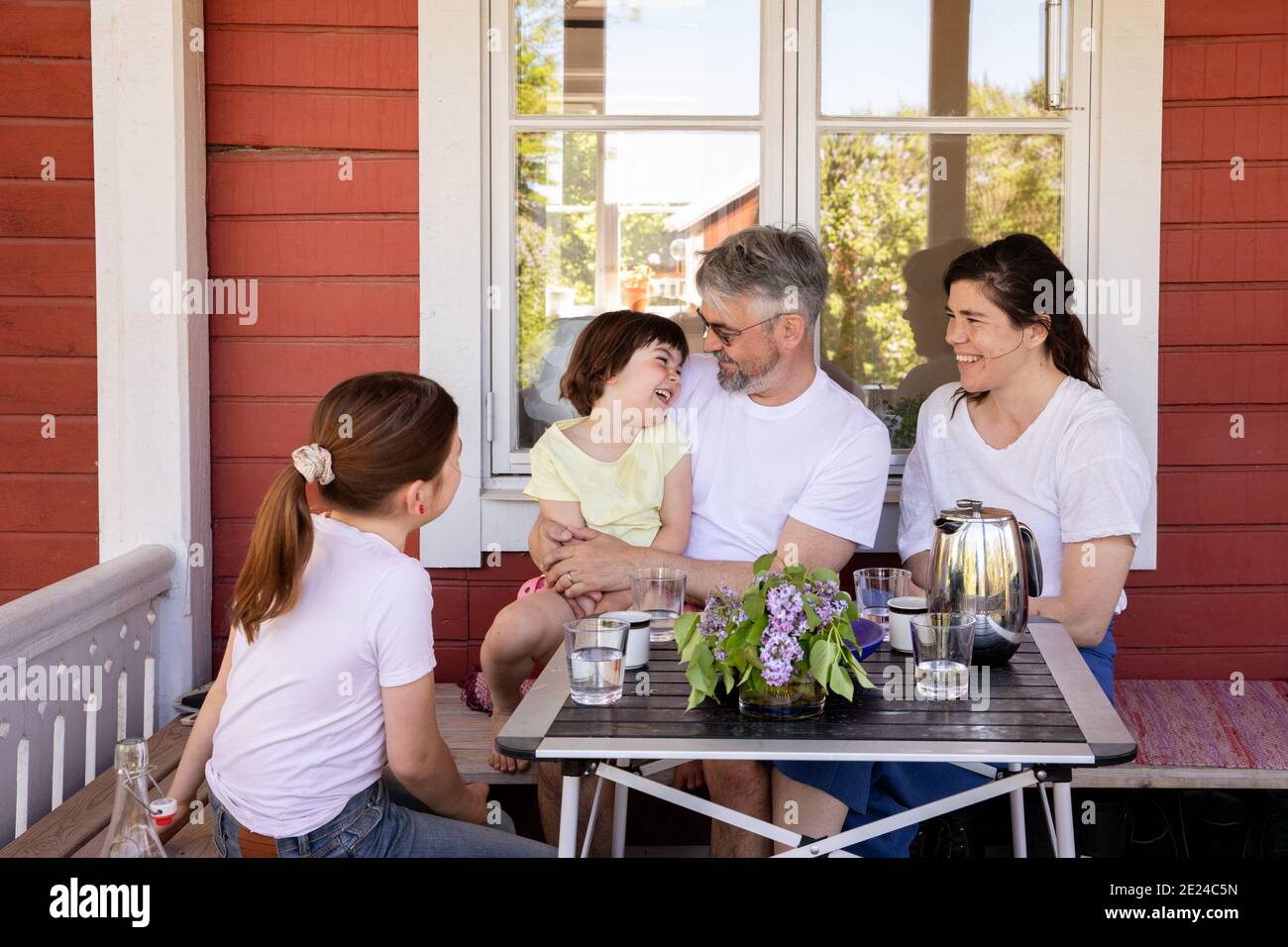 Parents avec deux filles assises devant la maison Banque D'Images