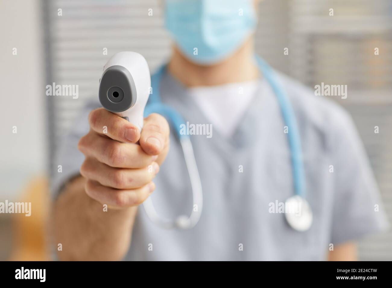 Gros plan d'un médecin masculin méconnaissable pointant le thermomètre infrarouge vers la caméra pendant le contrôle de la température à l'hôpital, copier l'espace Banque D'Images