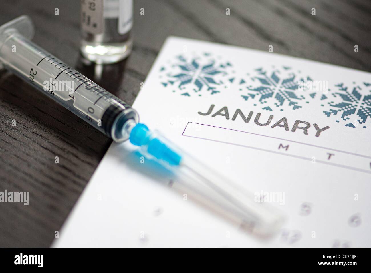 Seringue, flacon et calendrier avec mois de janvier sur une table noire prête à être utilisée. Antécédents de vaccin Covid ou coronavirus Banque D'Images
