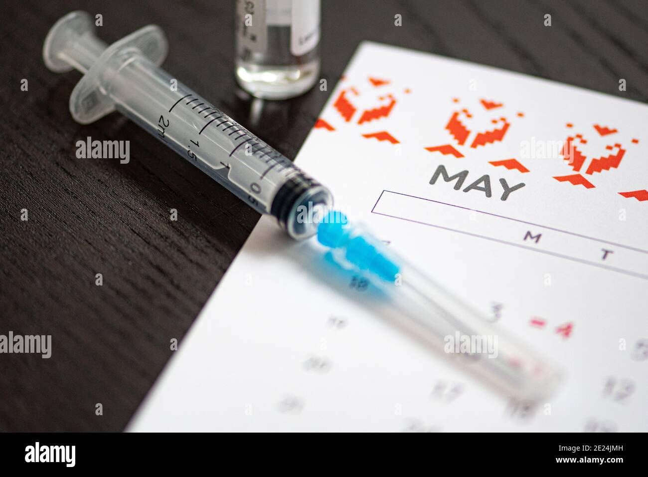 Seringue, flacon et calendrier avec mois de mai sur une table noire prête à être utilisée. Antécédents de vaccin Covid ou coronavirus Banque D'Images