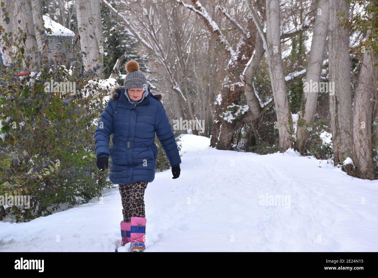 Une femme plus âgée enveloppée de chaleur dans une veste, des bottes et un chapeau marchant sur une route de campagne enneigée. Scène après la tempête de neige appelée Filomena en Espagne. Janvier 2021. Banque D'Images