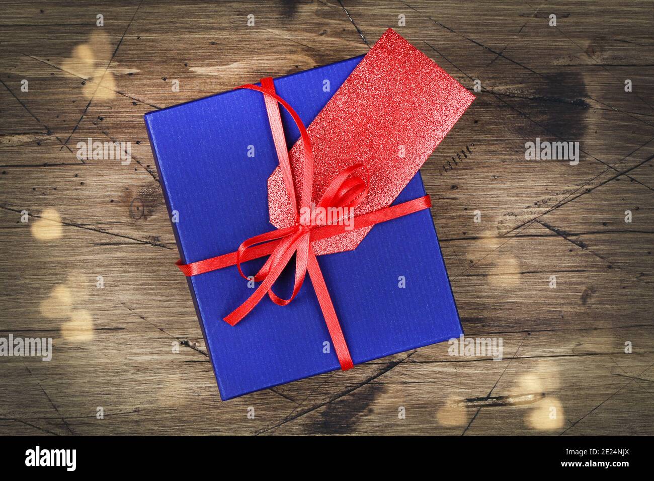 boîte cadeau bleue avec ruban rouge, étiquette cadeau vierge et bokeh sur fond en bois. vue du dessus. plan à plat Banque D'Images