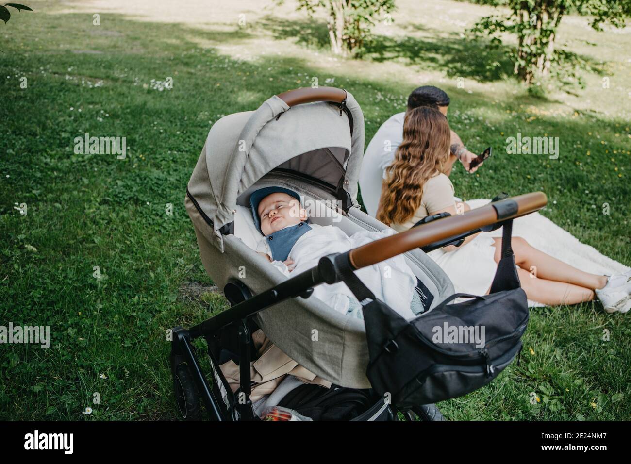 Bébé garçon dormant en pram, parents en arrière-plan Banque D'Images