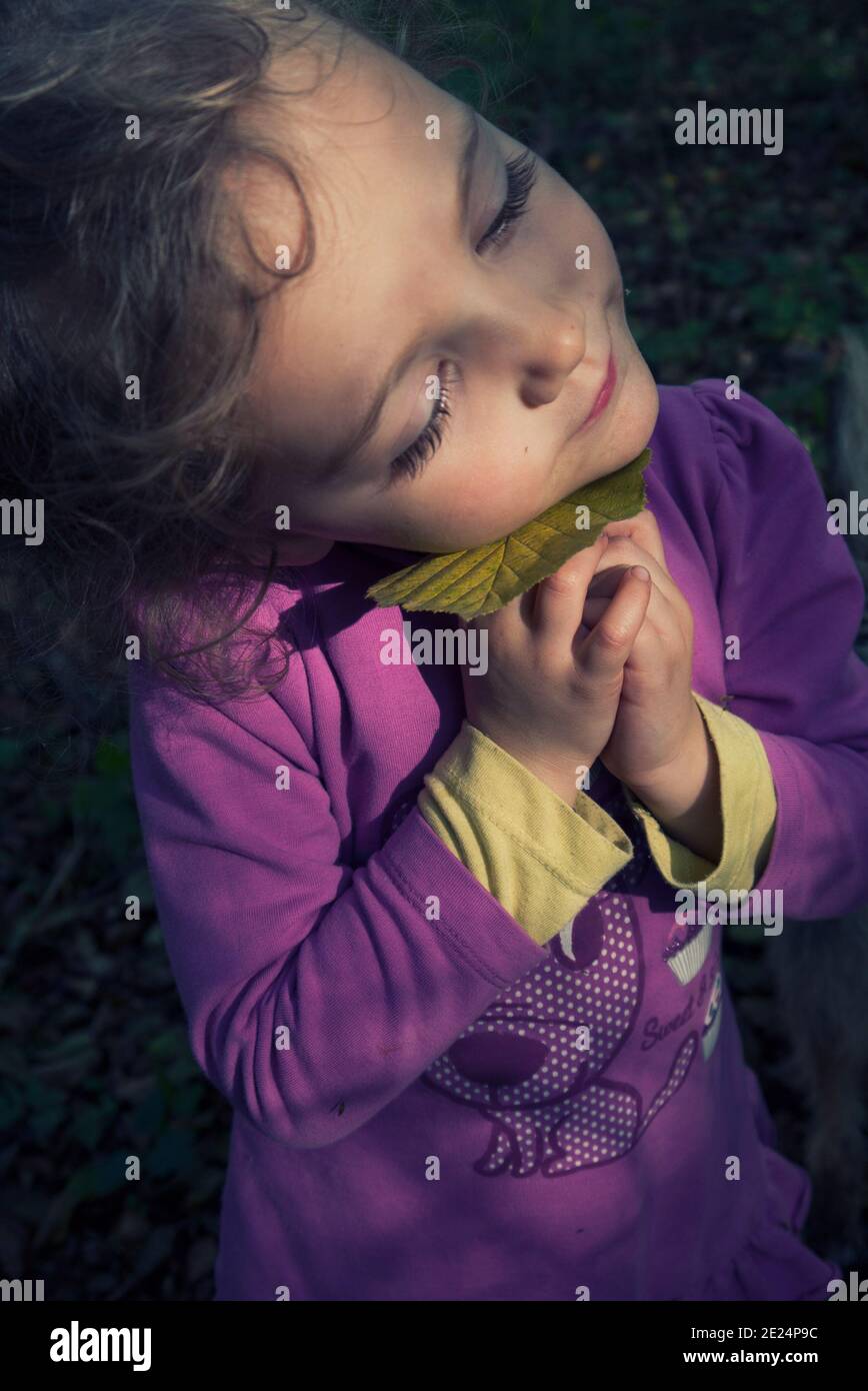 Fille souriante debout dans la forêt tenant une feuille contre son visage, la Pologne Banque D'Images