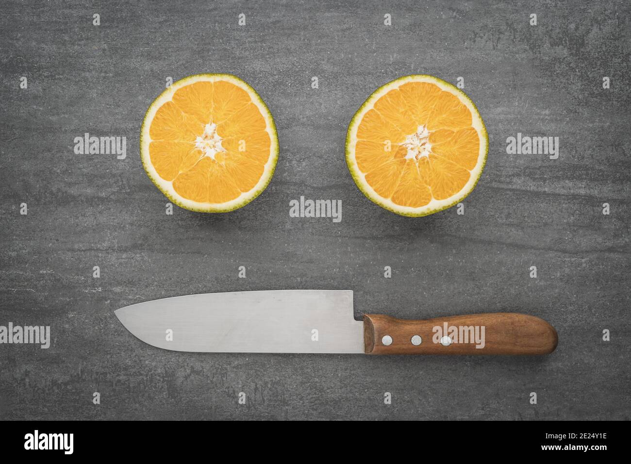Un visage souriant fait d'un couteau et d'oranges. Des agrumes sains, pleins de vitamines, coupés en deux. Banque D'Images
