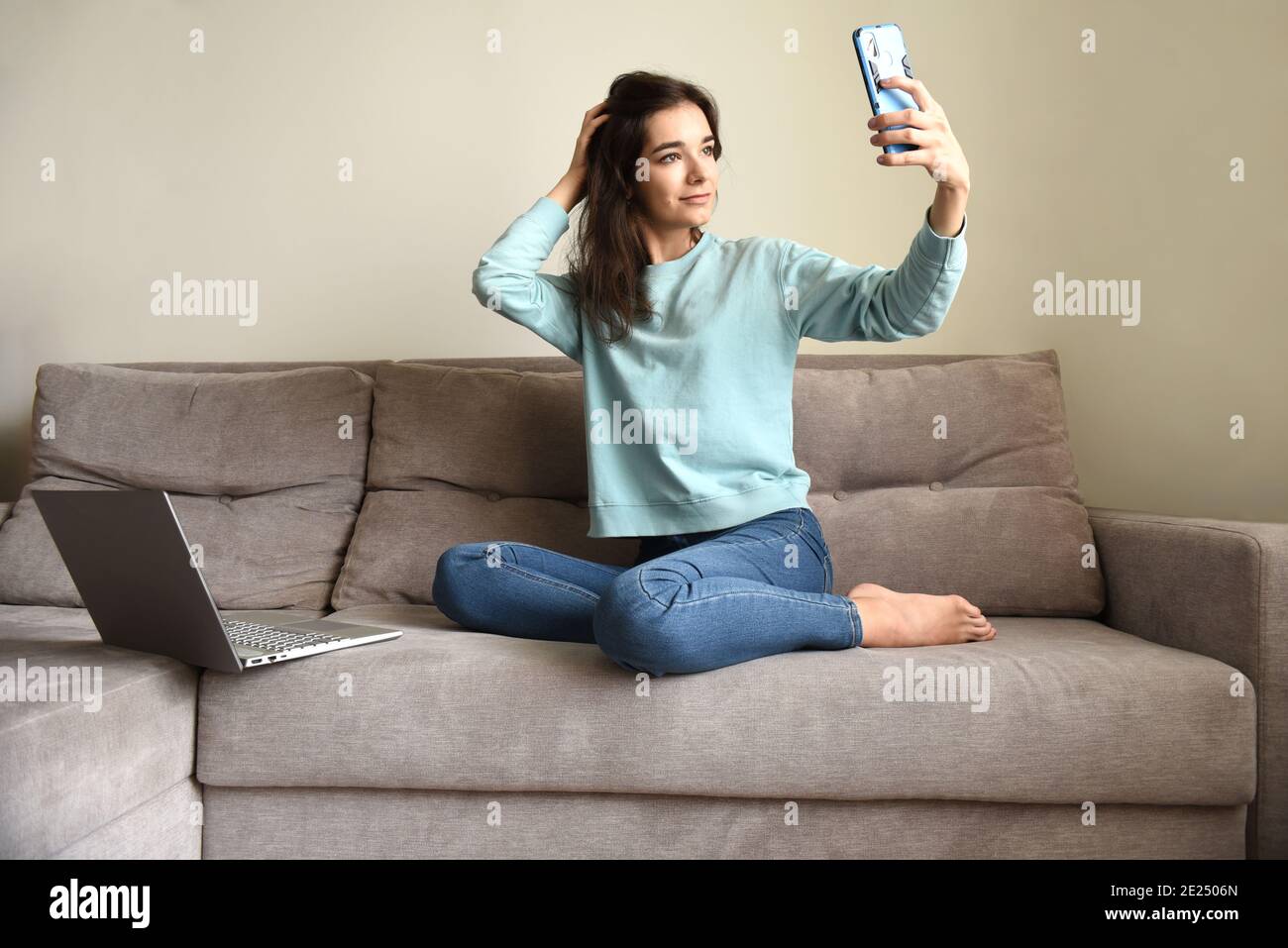 Jeune femme souriante prenant un selfie pour son profil. Elle est assise sur un canapé près d'un ordinateur portable à la maison. Verrouillage et datant en ligne concept Banque D'Images