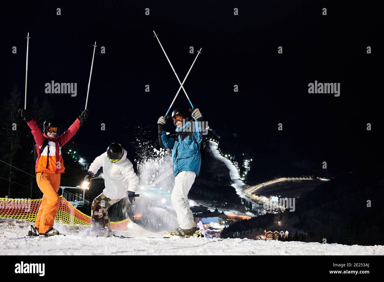Amis skieurs en hiver vestes et casques s'amuser à la station de ski en montagne en hiver, ski de nuit, pistes de ski éclairées sont en arrière-plan. Concept de mode de vie sain Banque D'Images
