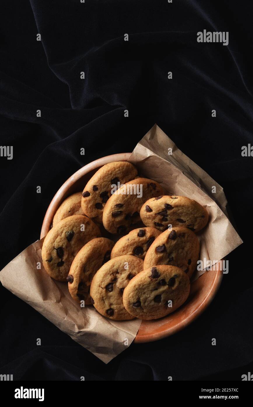 Photo en grand angle d'un bol en bois rempli de biscuits aux pépites de chocolat maison frais, sur un tissu noir avec espace de copie. Banque D'Images