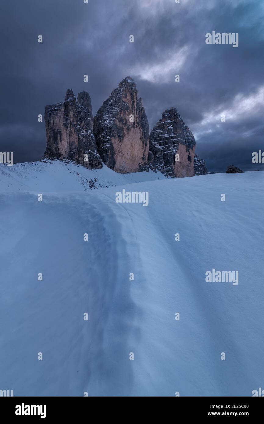 Une photo d'un sentier dans la neige en face de Tre Cime di Lavaredo, site classé au patrimoine de l'UNESCO dans les Dolomites italiens, sur un coucher de soleil nuageux Banque D'Images