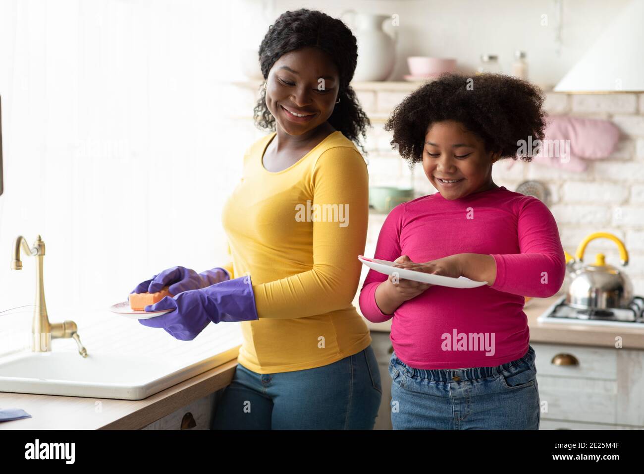 Petite Housekeeper. Mignon petite fille noire aider maman dans la cuisine, laver la vaisselle Banque D'Images