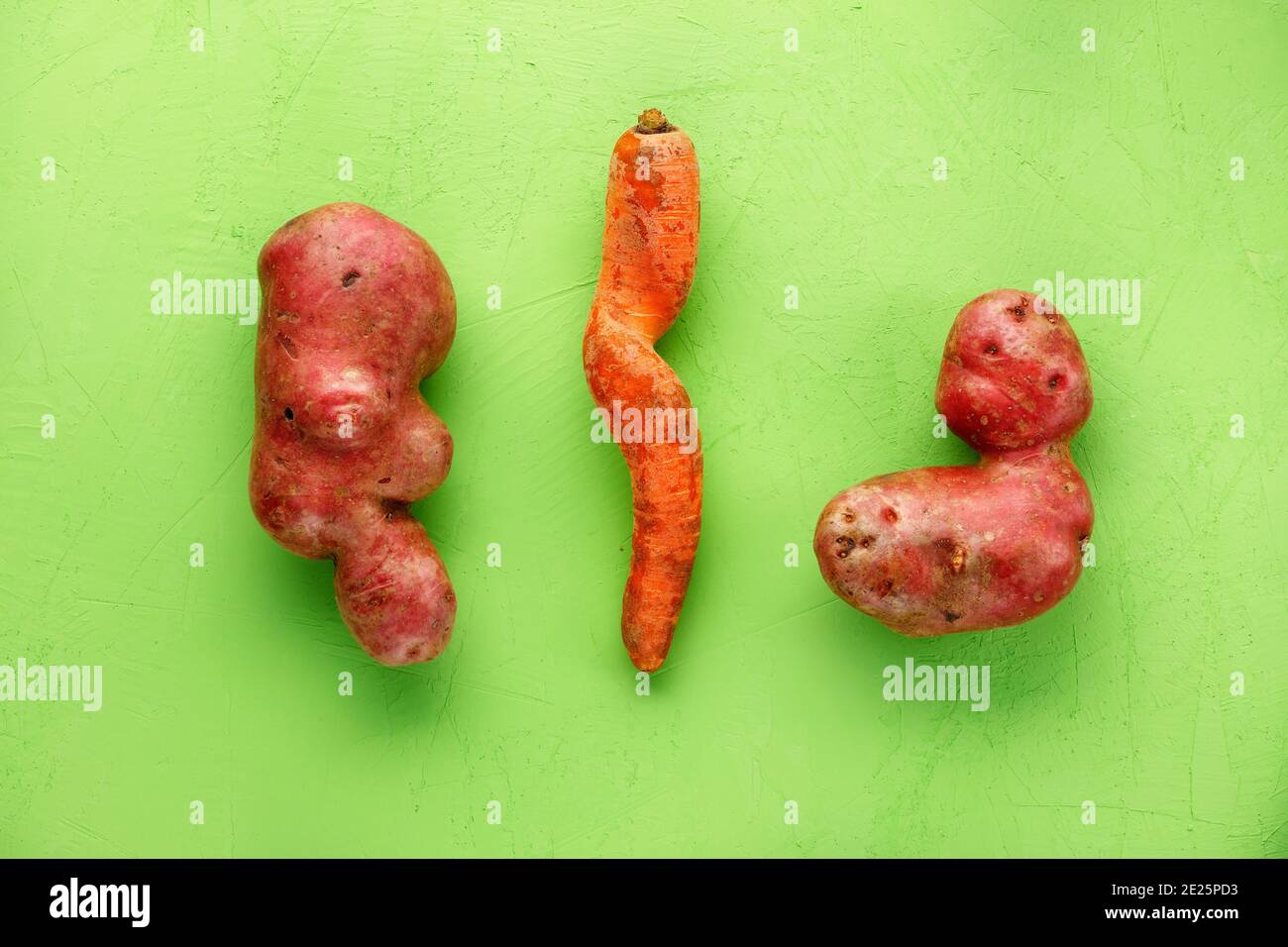 Des légumes rigoles, des pommes de terre grumeleuses et une carotte tordue sur fond vert. Notion : légumes grossiers ou déchets alimentaires. Vue de dessus, espace de copie. Banque D'Images