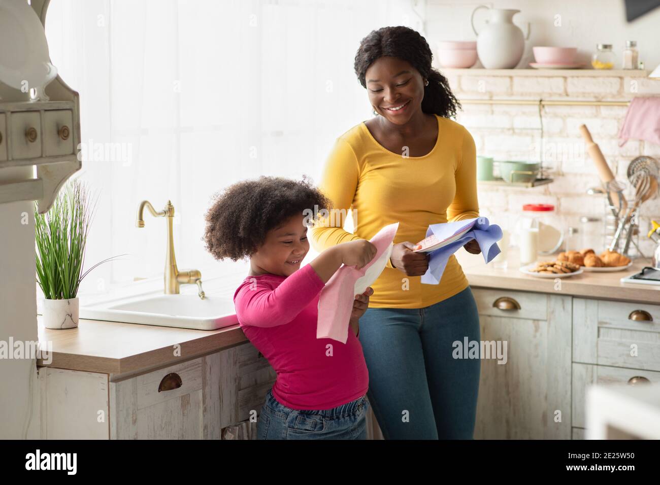 Mignon Afro-américaine fille aidant la mère avec la maison, Wiping plats dans la cuisine Banque D'Images
