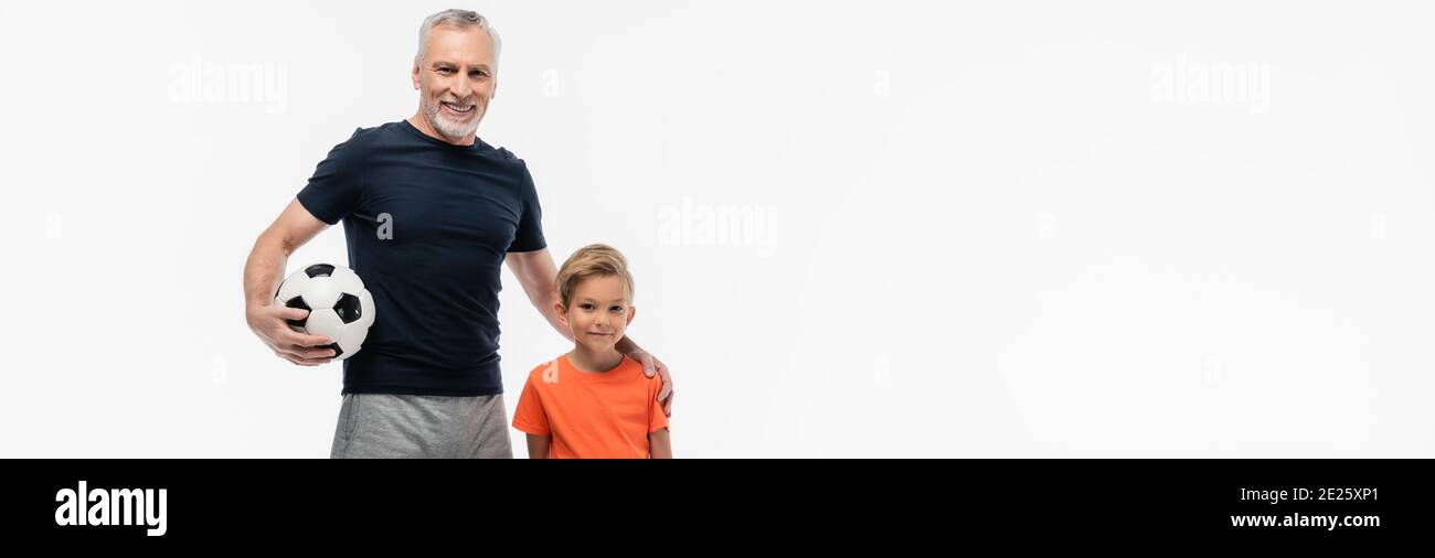 homme joyeux tenant la main sur l'épaule du petit-fils tout en tenant le ballon de football isolé sur blanc, bannière Banque D'Images