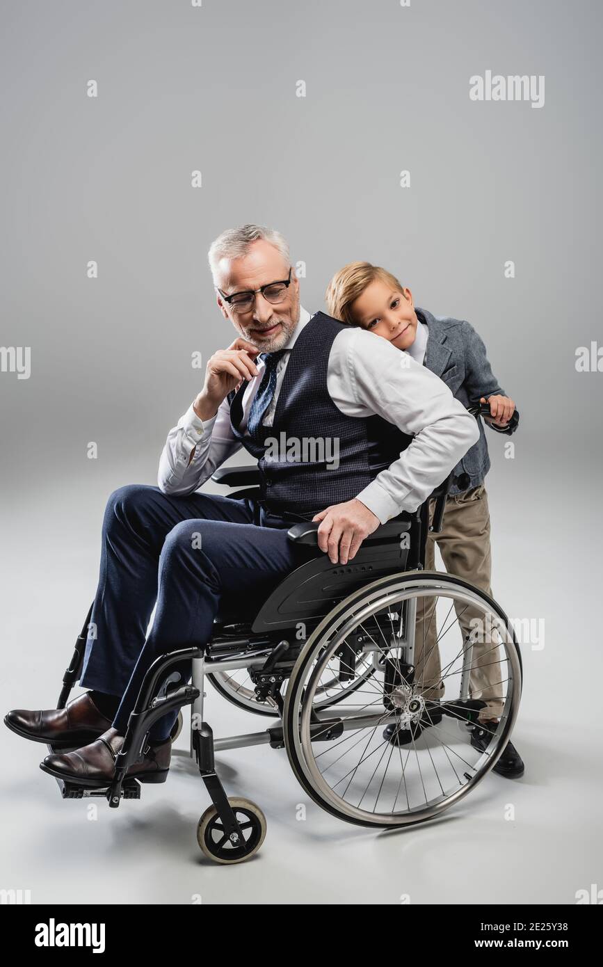 garçon souriant assis à l'arrière du grand-père en fauteuil roulant gris Banque D'Images