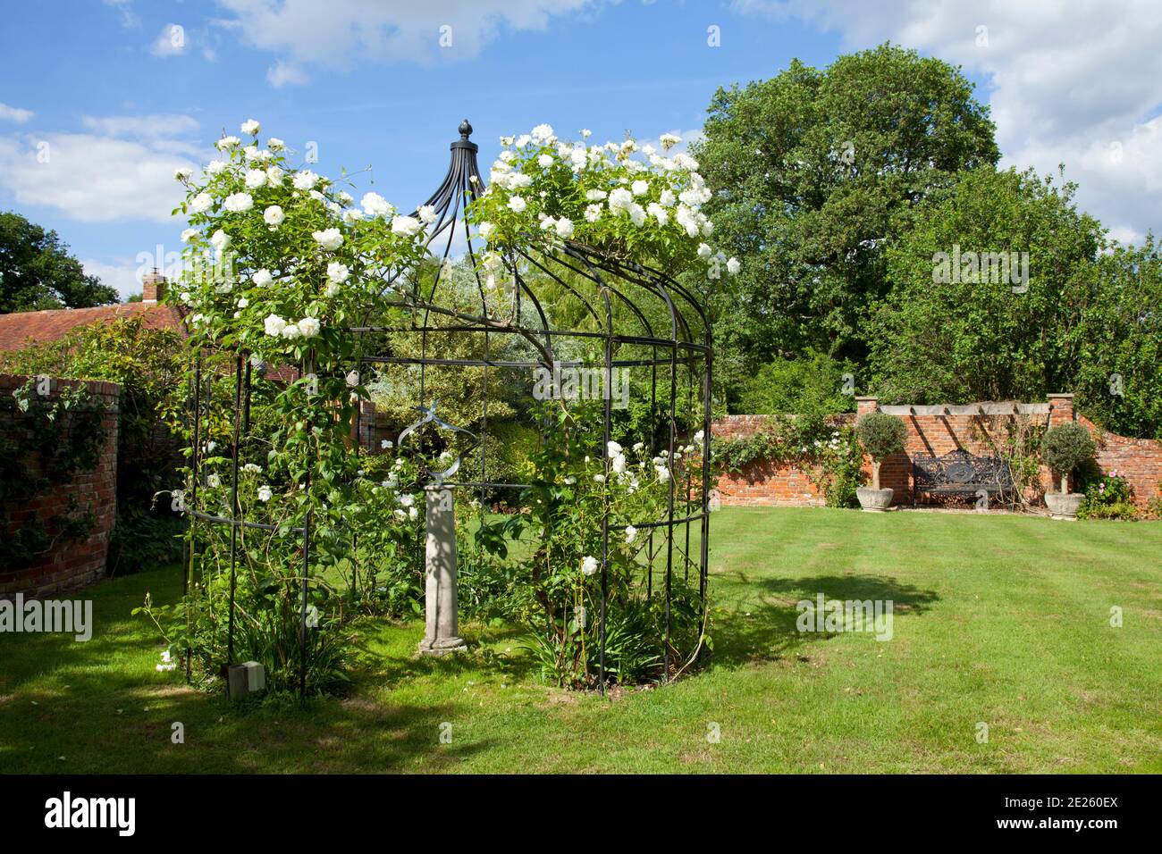 Tonnelle rose avec roses grimpantes blanches et sculpture en brique rouge jardin clos Banque D'Images