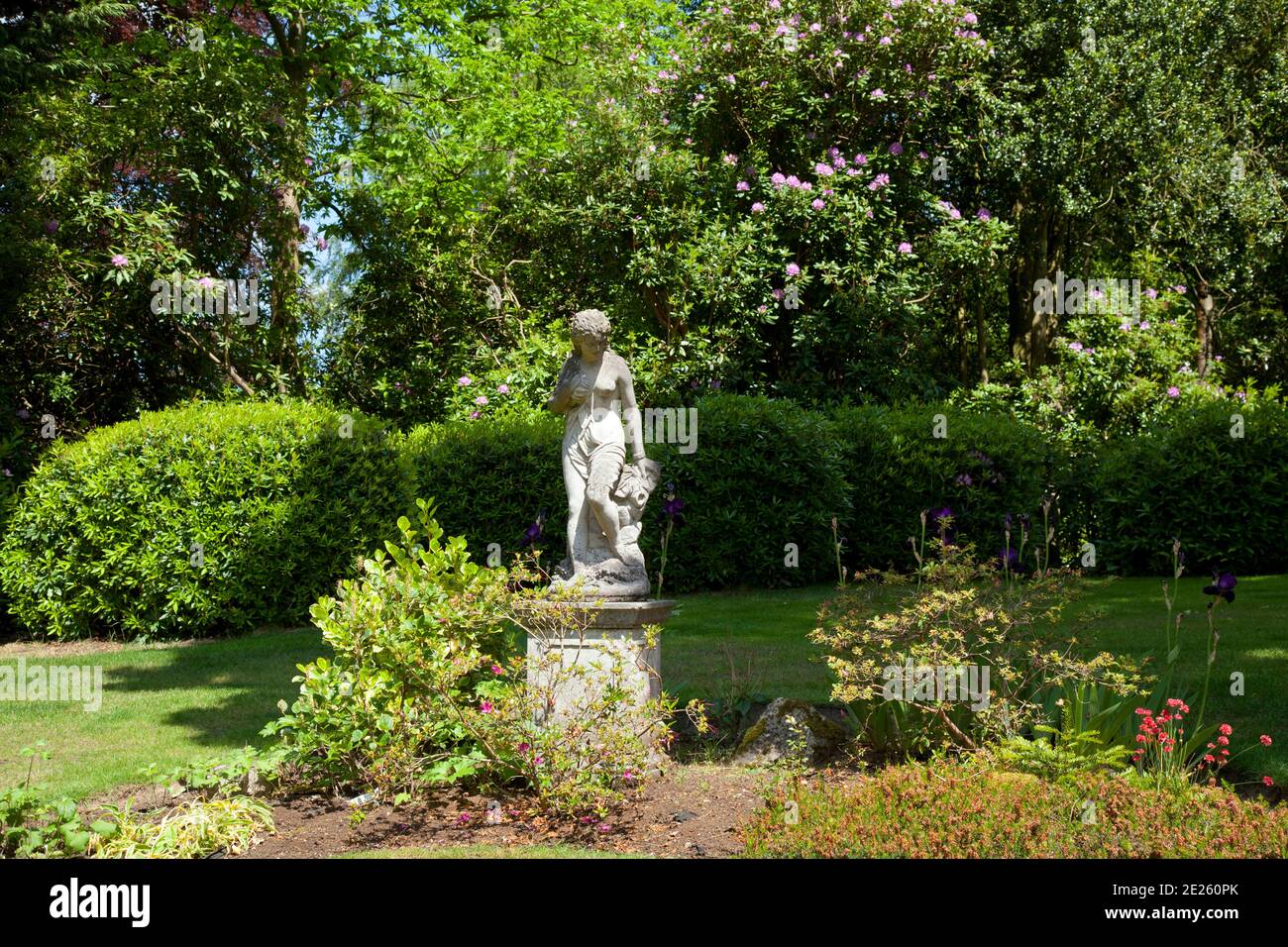Jardin mature avec statue en pierre sur plinthe semi-nue femme Banque D'Images