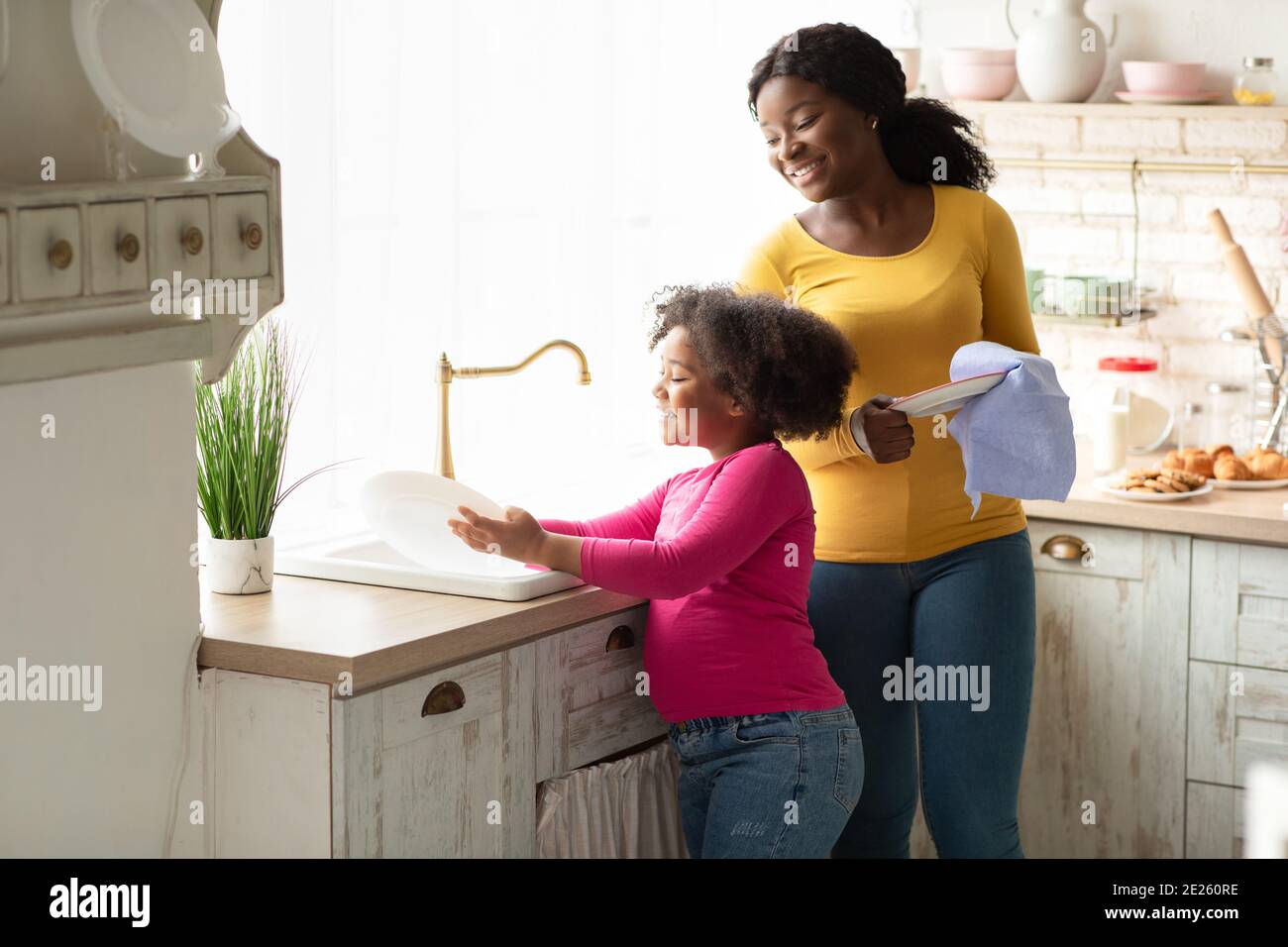 Petit casque. Mignonne de lave-vaisselle de petite fille noir avec maman dans la cuisine Banque D'Images