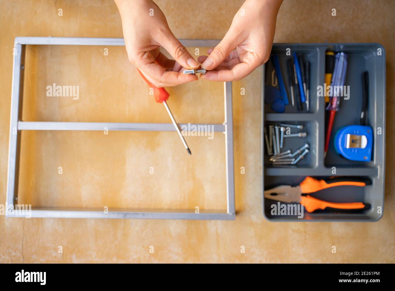 femmes réparant un objet métallique ancien. tournevis rouge et jaune, pince  orange, vis et mètre ruban bleu dans la boîte à outils. banc d'atelier en  bois jaune Photo Stock - Alamy