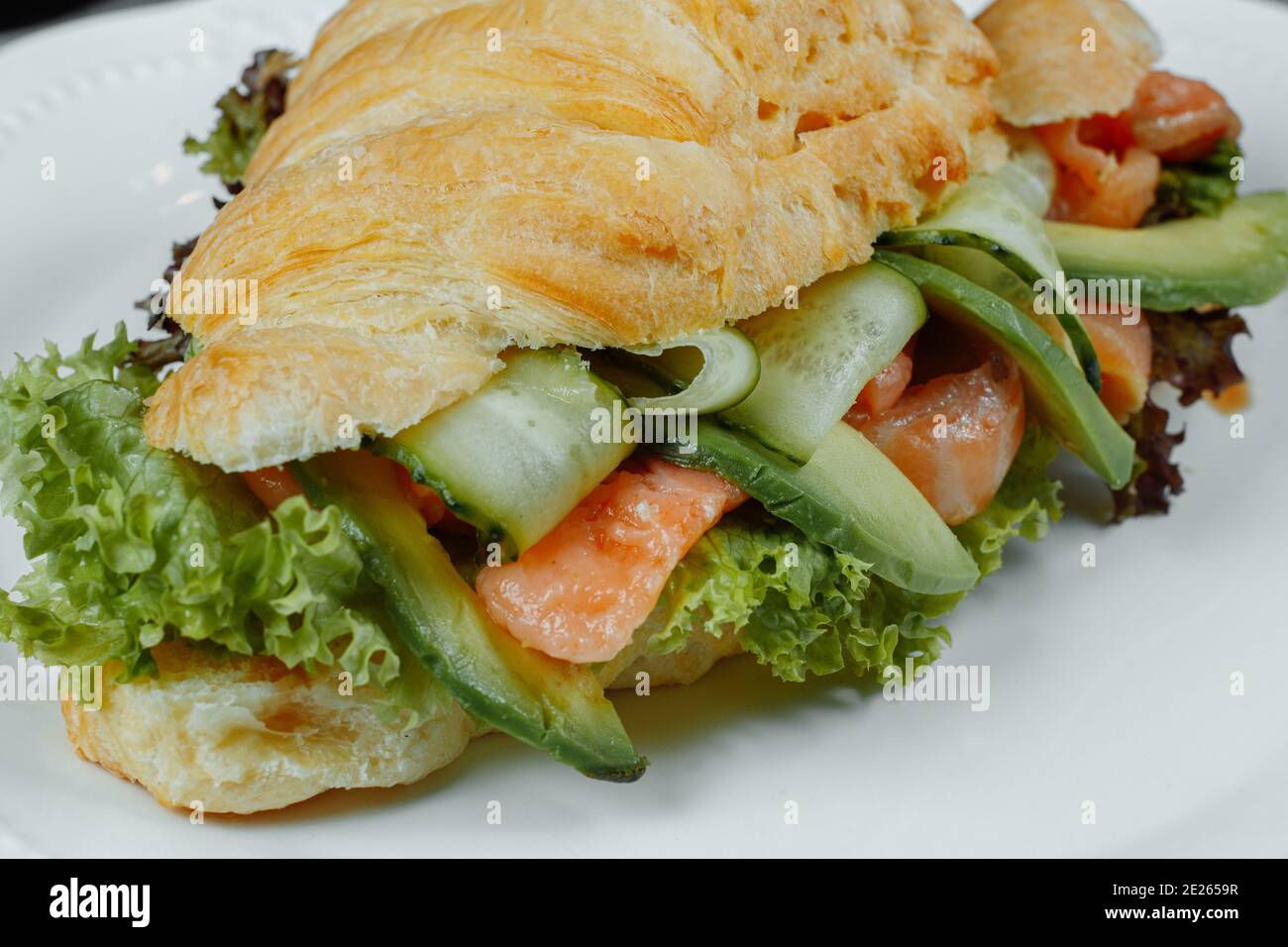 Sandwich croissant avec poisson rouge, avocat, légumes frais et arugula sur fond noir de pierre. Concept d'alimentation saine. Banque D'Images