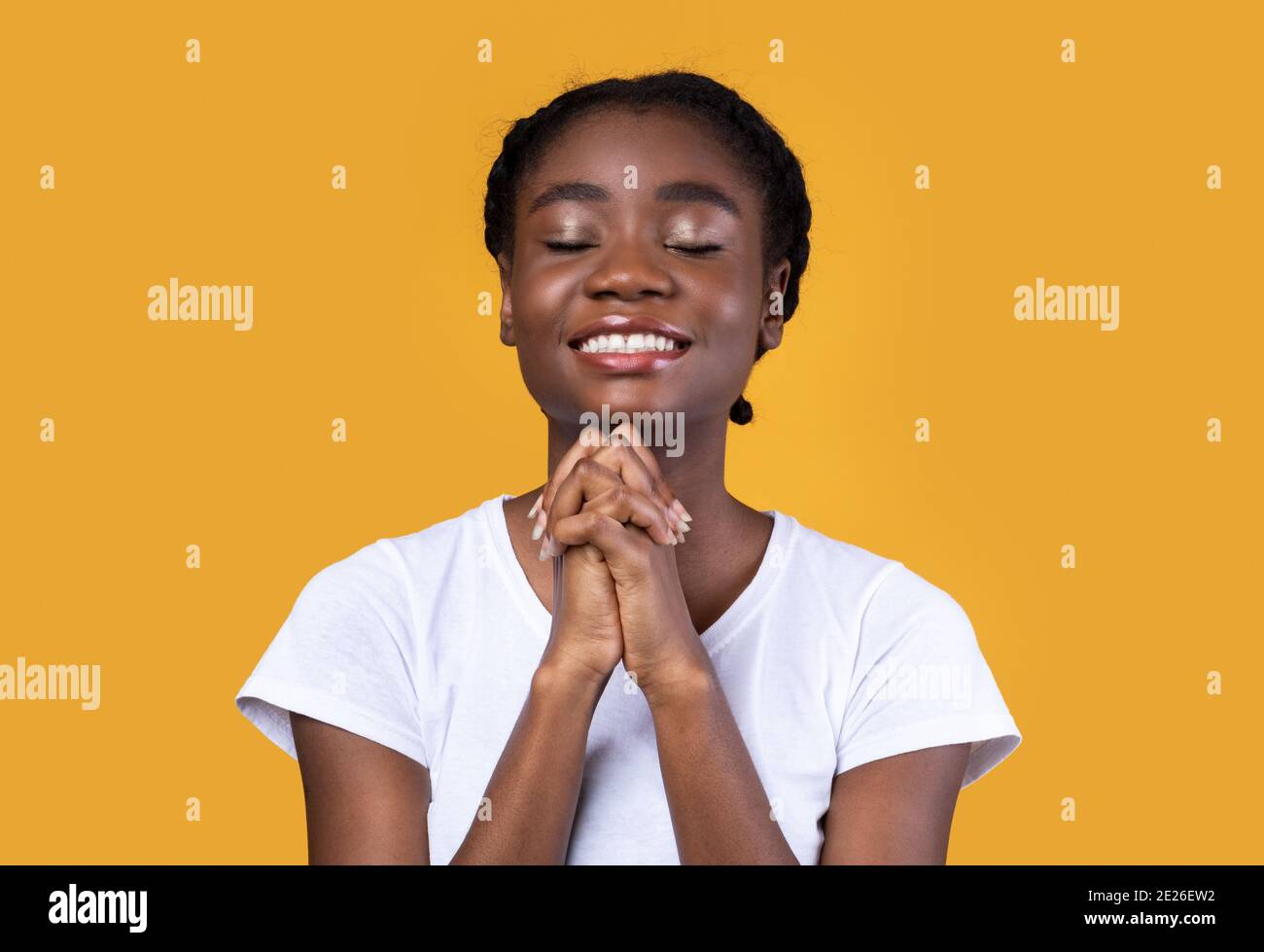 Femme afro-américaine priant debout sur fond de studio jaune Banque D'Images